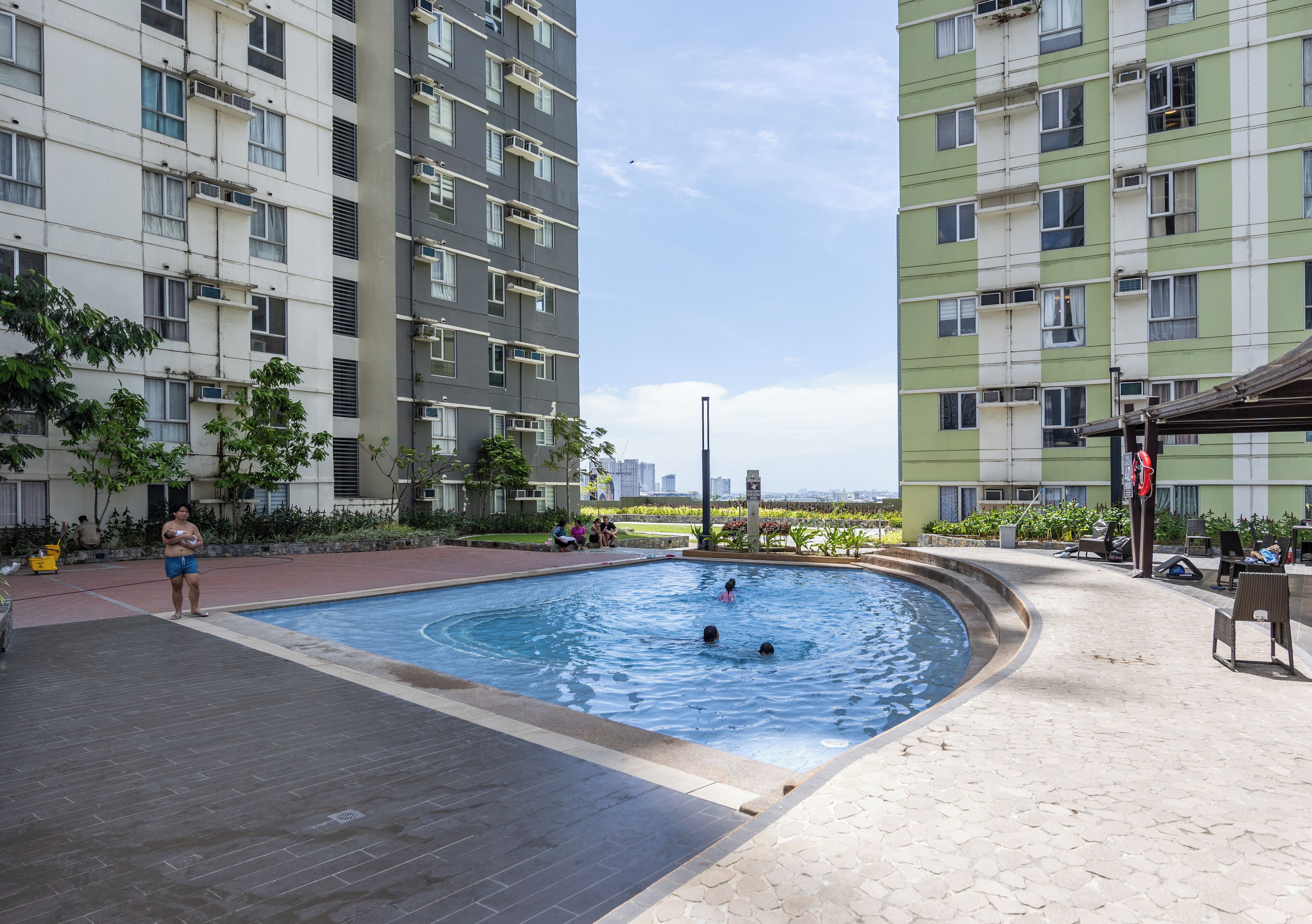 A swimming pool surrounded by apartment buildings, with a few people around the pool area.