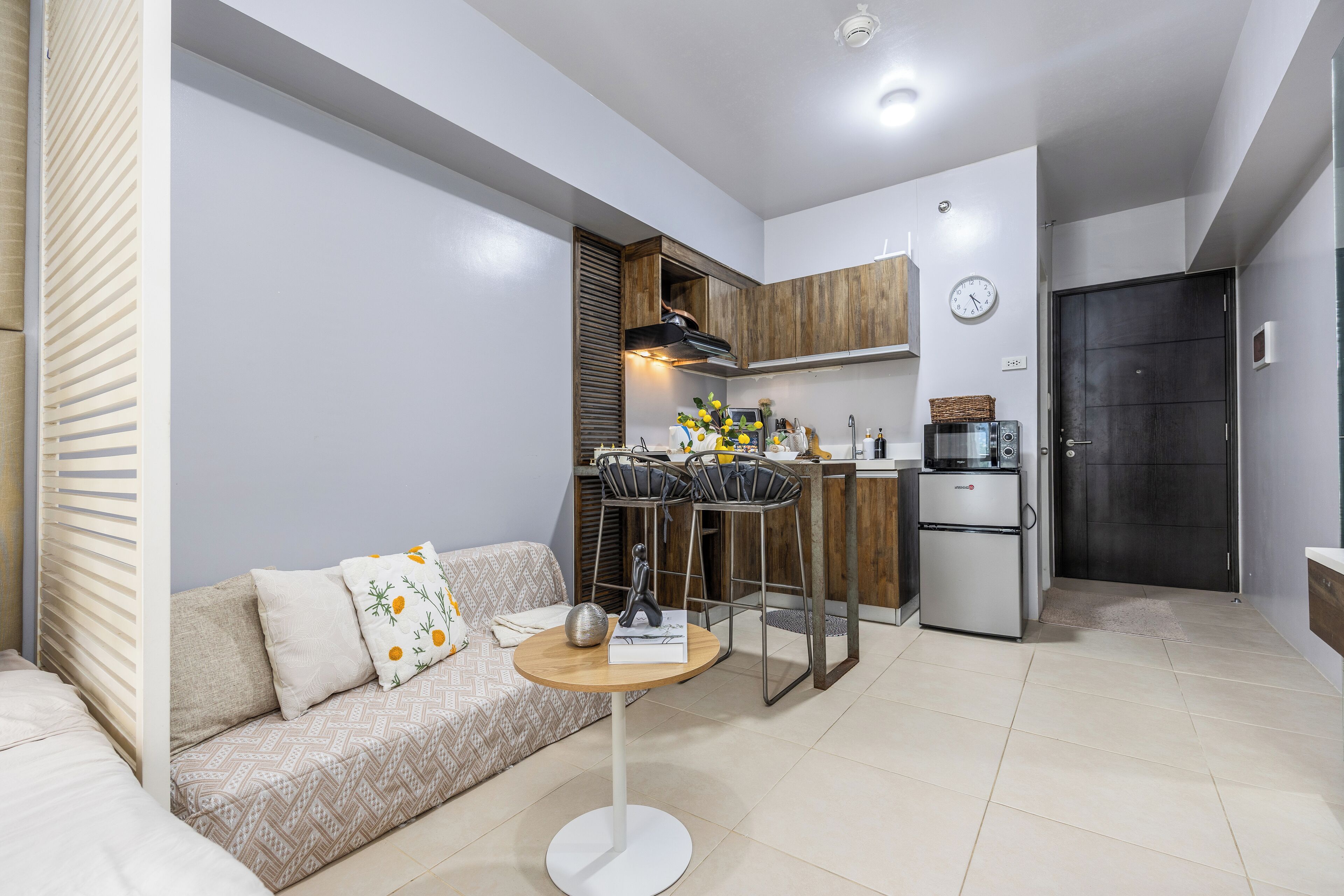 A compact living space with a kitchenette, a sofa with patterned cushions, a small round table, and a dining area with metal chairs.
