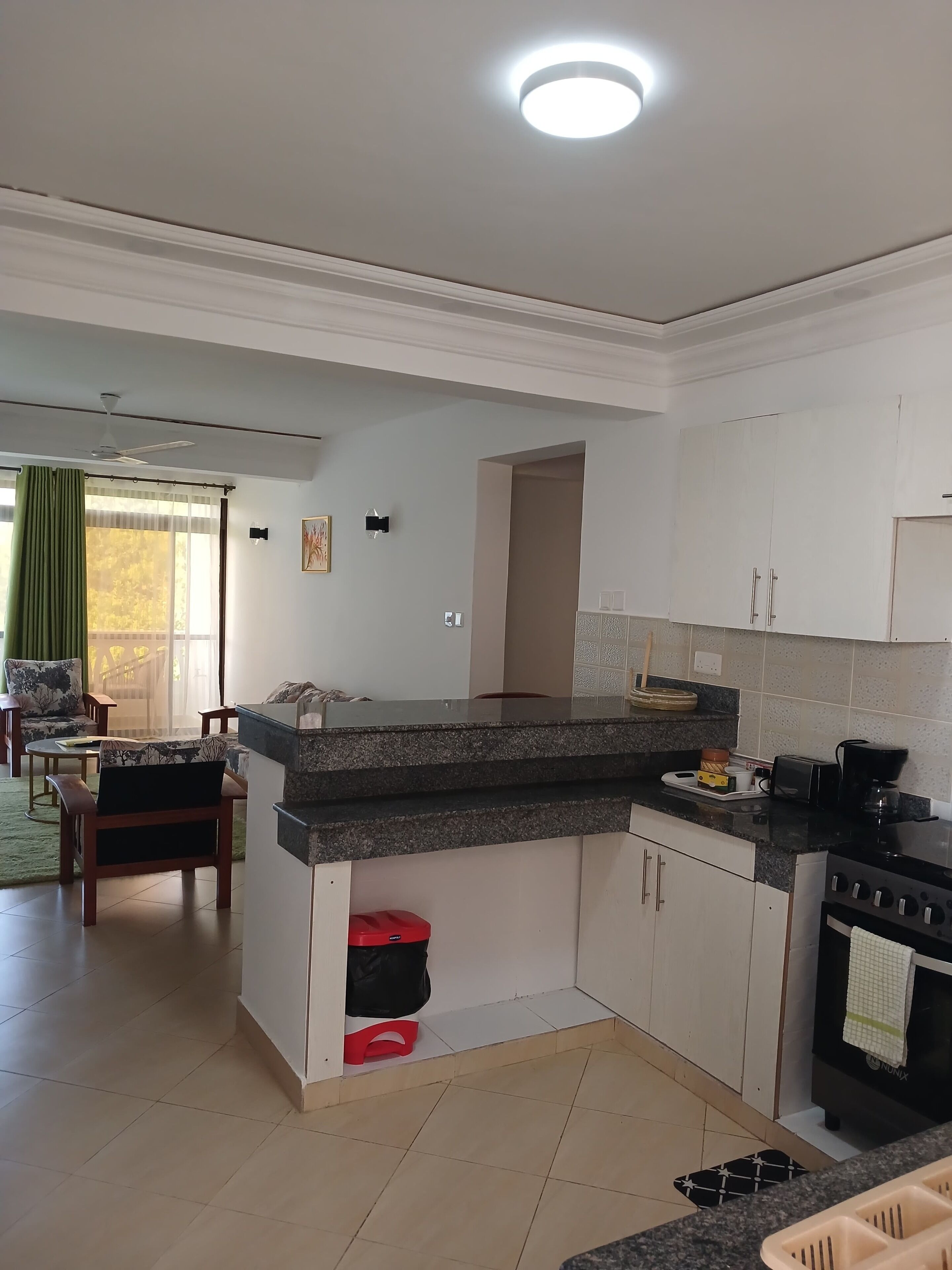A modern kitchen with white cabinets, a granite countertop, and a built-in oven. There is a dining area with a table and chairs, and a view of the outdoors through a window.