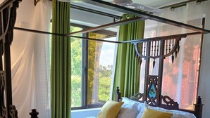 Een bed met hemel, groene gordijnen en uitzicht op groen.