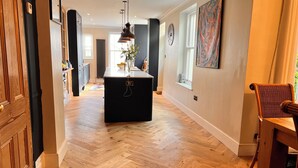 A spacious hallway with wooden flooring, a central island, and a dining area with a wicker chair. - Home in Appledore with own parking and Hot Tub. Dogs welcomed (Appledore)