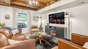 Un salón con sofá de cuero, una mesa de centro de vidrio, televisor montado en la pared y chimenea.