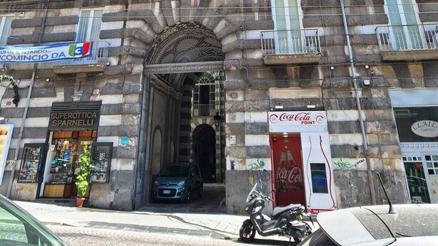 Un edificio de varios pisos con una entrada central, balcones y varias tiendas en la planta baja.