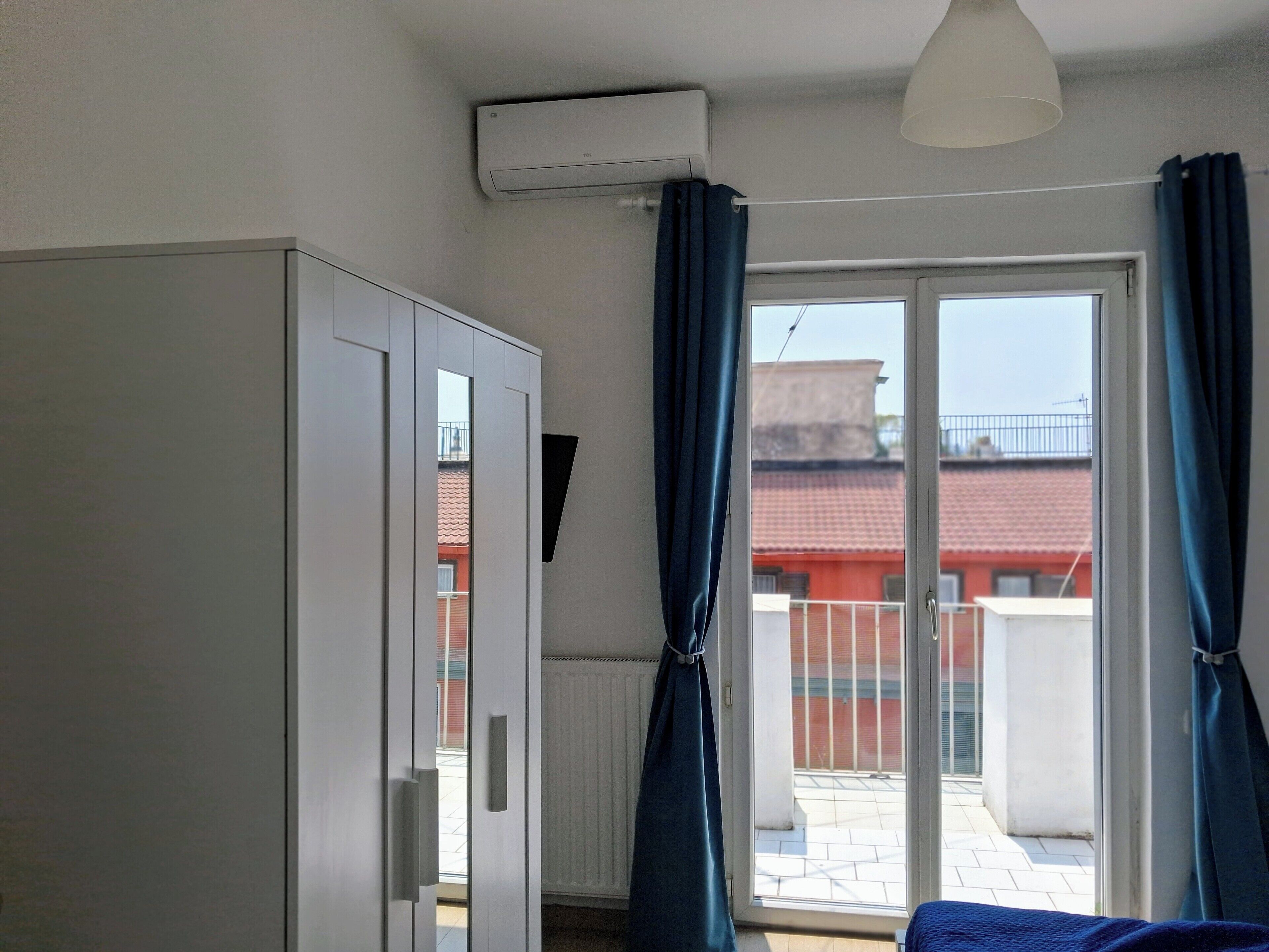 Een kamer met een schuifglasdeur naar een balkon, een witte kledingkast en een luchtverkoeler aan het plafond.