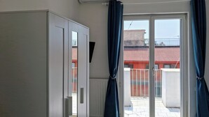 Una habitación con puerta de vidrio corrediza a un balcón, un armario blanco y aire acondicionado instalado en el techo.