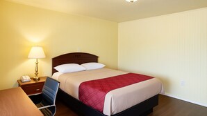 A hotel room with a bed, a desk, a lamp, and a chair. - Budget Motel Granite City/St Louis Area (Granite City)