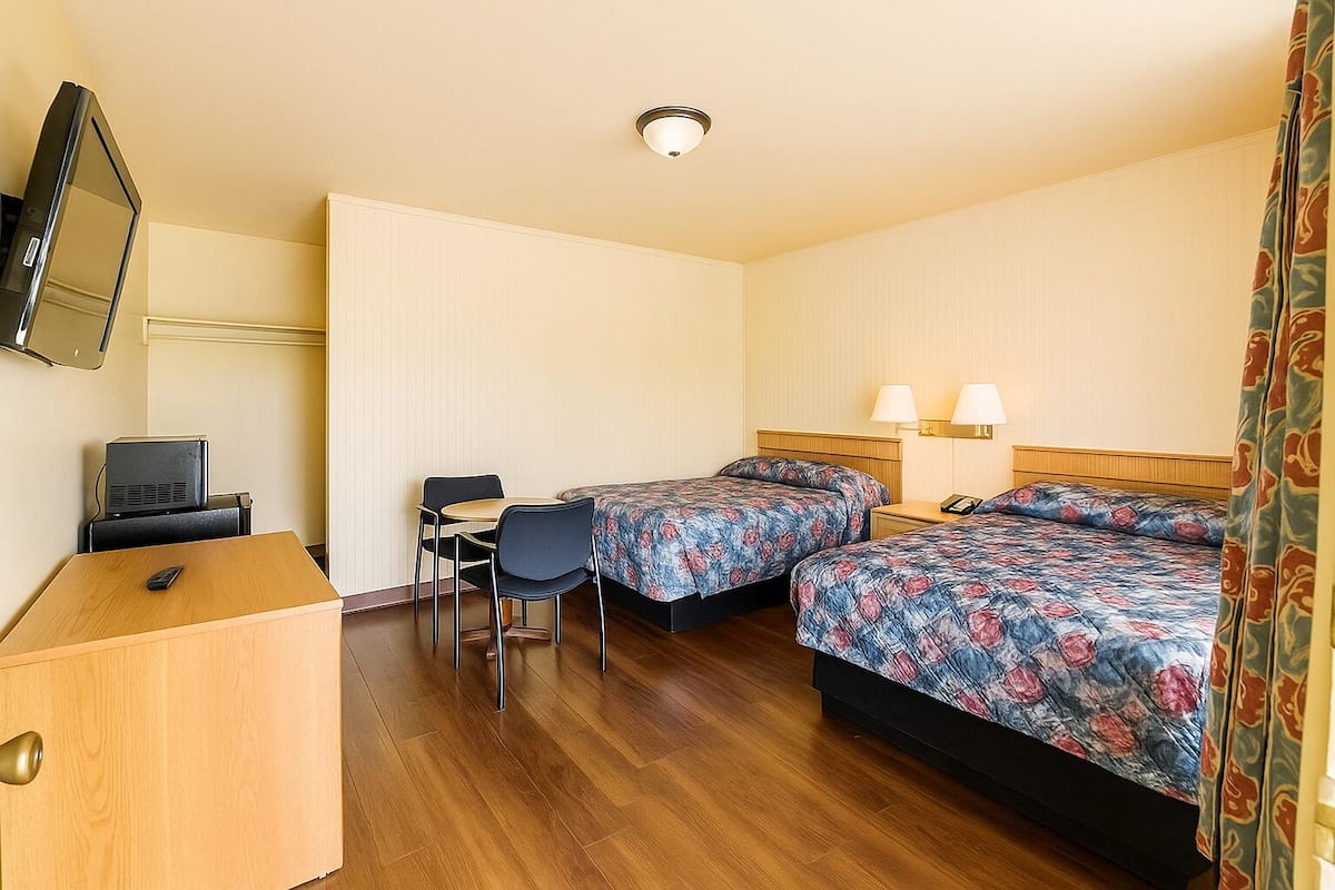 A hotel room with two beds, a desk, a chair, a television, and a telephone.