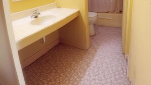 A bathroom with a yellow wall, a white sink, a mirror, and a toilet. - Budget Motel Granite City/St Louis Area (Granite City)