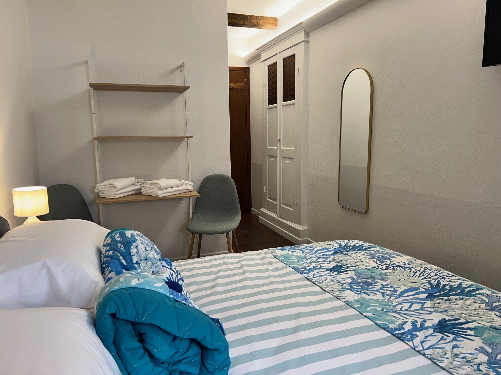 Een hotelkamer met een bed, een stoel, een plank met handdoeken, een kast en een spiegel.