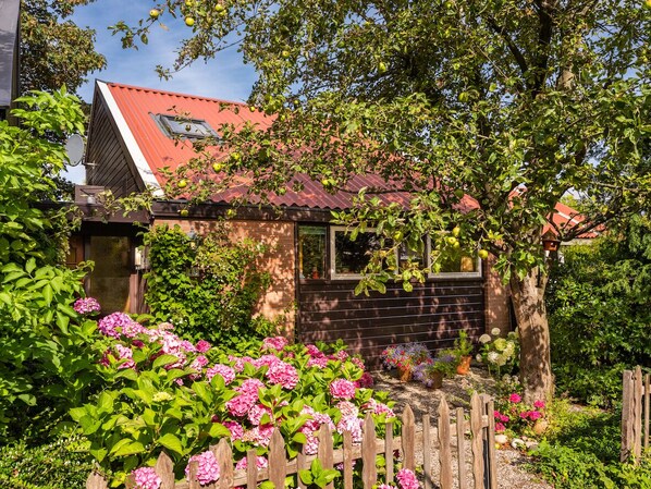 A house with a red roof, surrounded by a wooden fence and lush greenery.