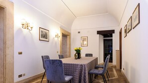 A dining area with a table set for four, surrounded by chairs, in a hallway with white walls and framed pictures.
