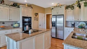 Una cocina moderna con armarios blancos, encimeras de granito, electrodomésticos de acero inoxidable y una isla central.