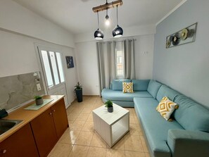 A modern living room with a sofa, a coffee table, a kitchen area with cabinets, and a dining table.