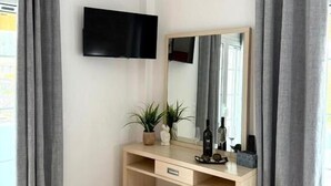A modern bedroom with a wooden desk, a flat-screen TV, a large mirror, and grey curtains. - Casa Damour  (Sidari)