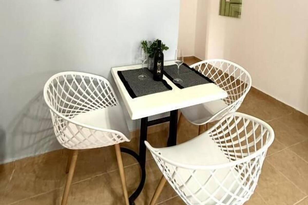 A dining area with a white table and four white chairs, a bottle of wine, and a small plant on the table.