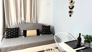 A room with a bed, a white chair, a small table with a bottle and glasses, and a wall-mounted light fixture. - Casa Damour  (Sidari)