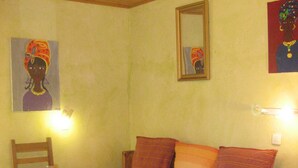 Une pièce avec un plafond en bois, une table ronde sur laquelle se trouvent un bol et un panier, un canapé avec des coussins, et des œuvres d’art murales, notamment un miroir encadré et un tableau.