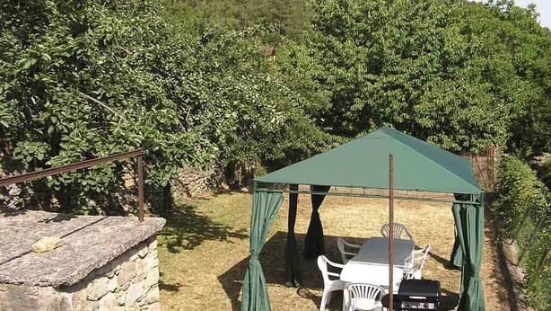 Un espace extérieur aménagé, abrité et doté de tables et de chaises, entouré d’un mur de pierre et d’une végétation luxuriante.