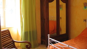 Une chambre avec un lit en bois, un rideau vert, une armoire en bois et une chaise.