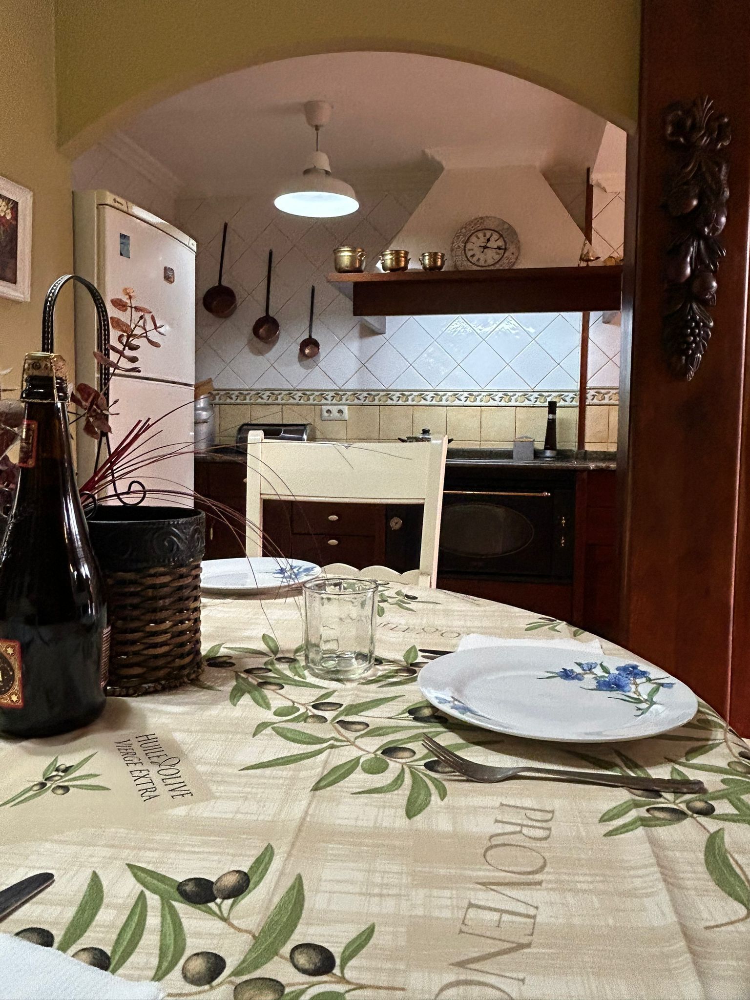 Un comedor con una mesa dispuesta para dos personas, una botella y un vaso sobre la mesa.