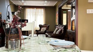 A dining area with a table set for four, a vase with flowers, and a view of a living room with a sofa and a window. - Cariño BBQ House - Casa Senen (Cariño)