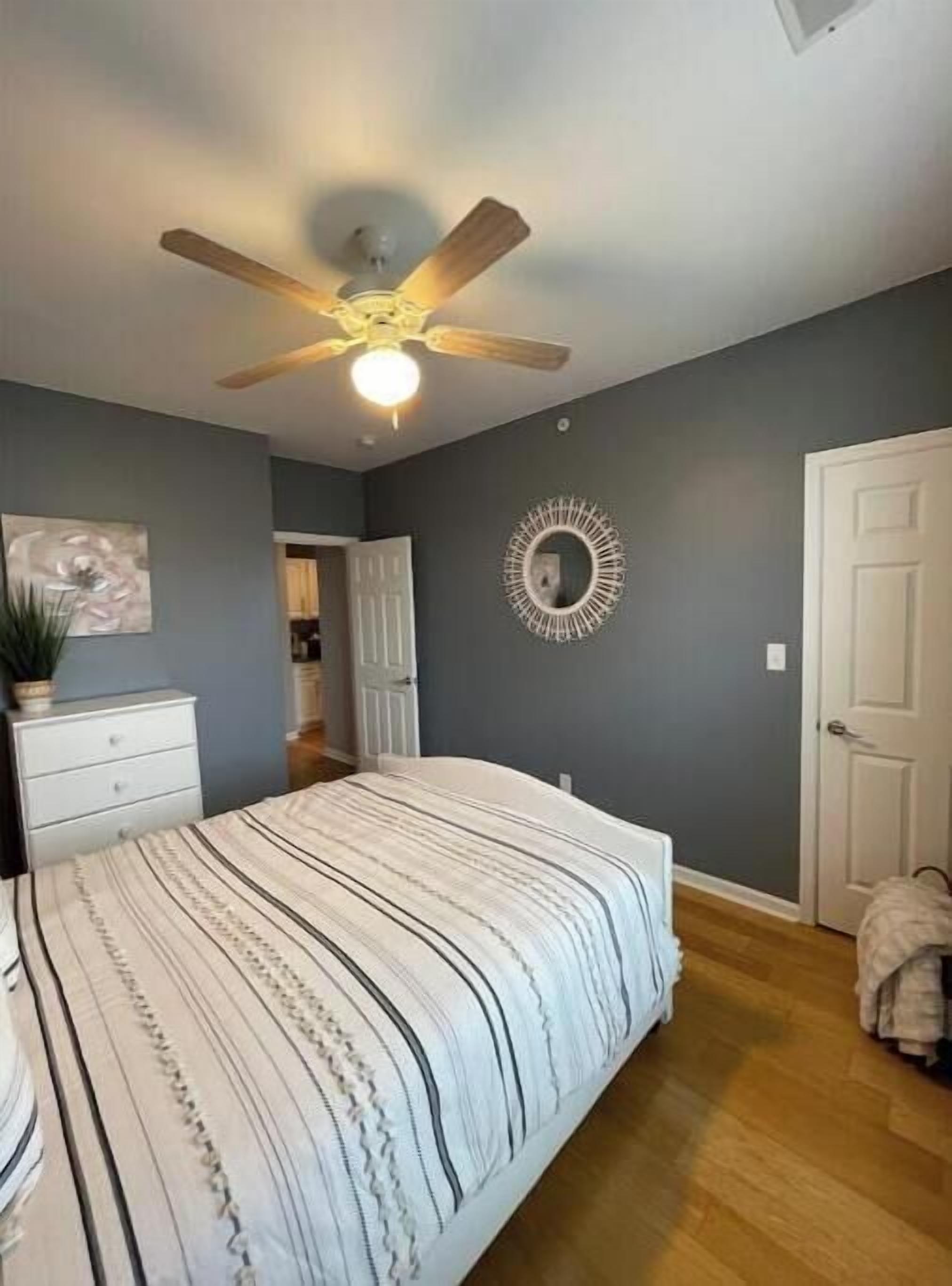A bedroom with a bed, a ceiling fan, a mirror, and a door.