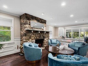 Sala de estar com lareira de pedra, poltronas estofadas em azul e mesa de centro redonda.