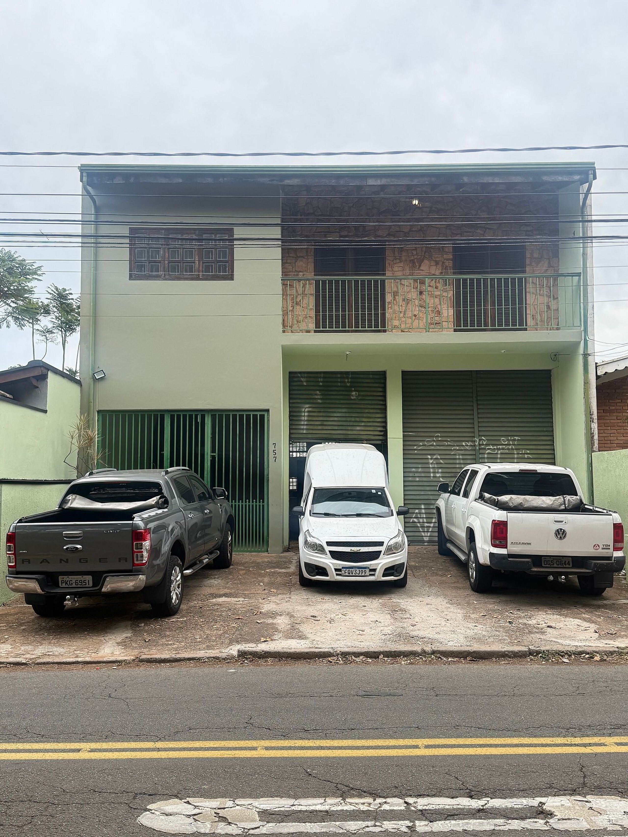 Tres vehículos estacionados frente a un edificio con fachada verde y una puerta de garaje.