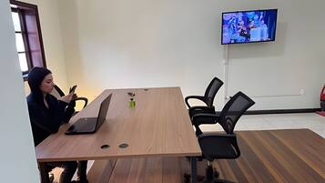 Un salón de conferencias con una larga mesa, sillas negras, una computadora portátil y una televisión en la pared.