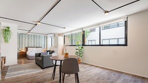 A modern living room with a sofa, a dining table, and chairs. There are potted plants and a large window providing natural light. - VH | Condesa nice loft with roof terrace + GYMNASIUM | 248 (Ciudad de México)