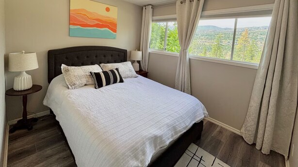 Un dormitorio con cama, mesita de noche, lámpara, un cuadro y ventana con cortinas.