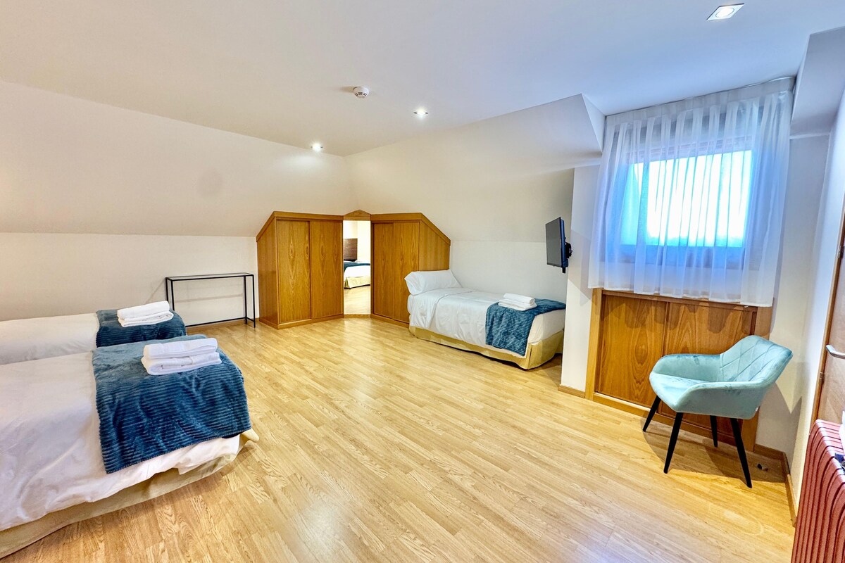 A hotel room with two beds, a wooden wardrobe, a small table, and a chair.
