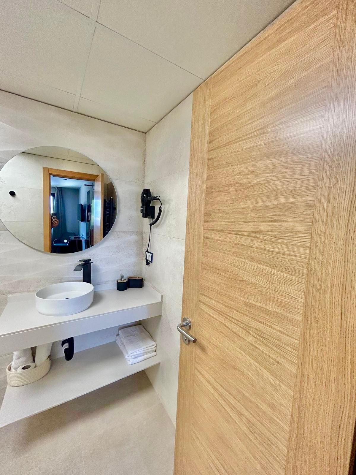 Un baño con un lavamanos blanco, un espejo redondo y una puerta de madera.