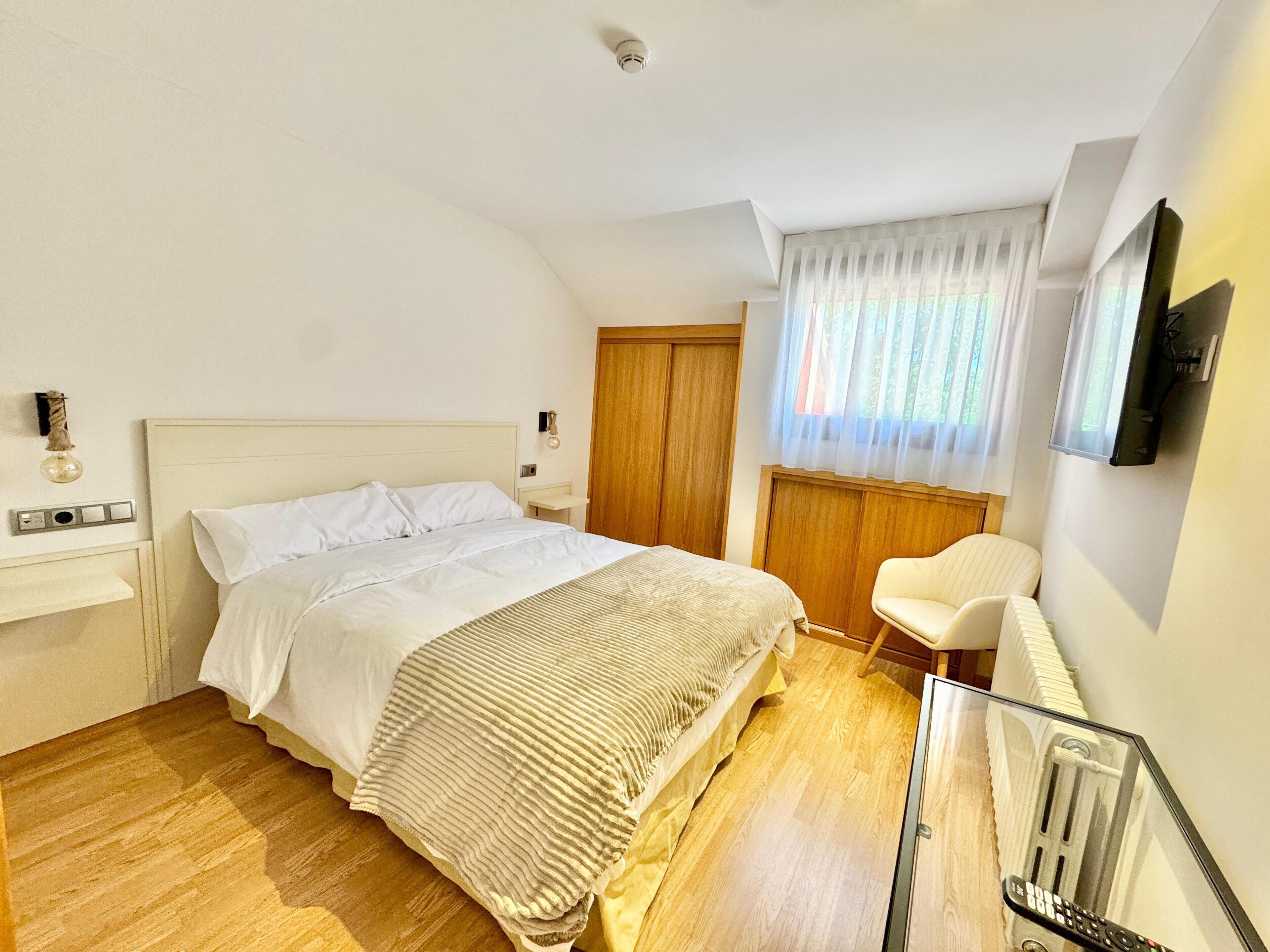 A bedroom with a bed, bedside table, chair, and a TV mounted on the wall.