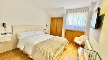 A bedroom with a bed, bedside table, chair, and a TV mounted on the wall.