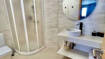 A modern bathroom with a glass-enclosed shower, a round mirror, and a white sink.
