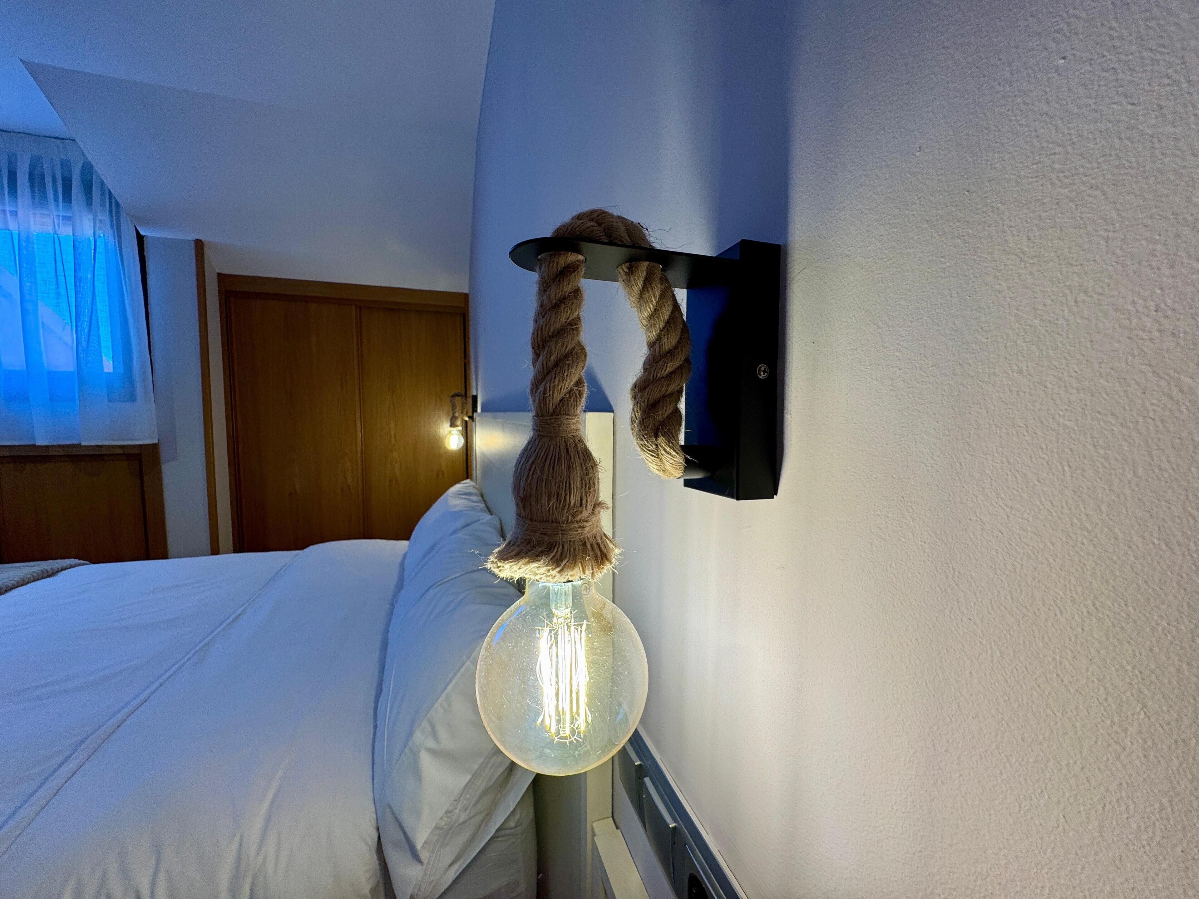 A bed with a headboard, a wall-mounted lamp, and a wooden door in the background.