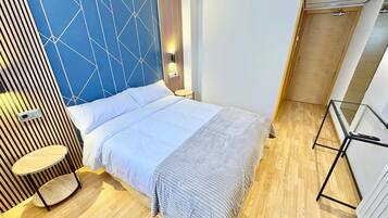 A modern bedroom with a geometric-patterned headboard, a round bedside table, and a glass table with a remote control.