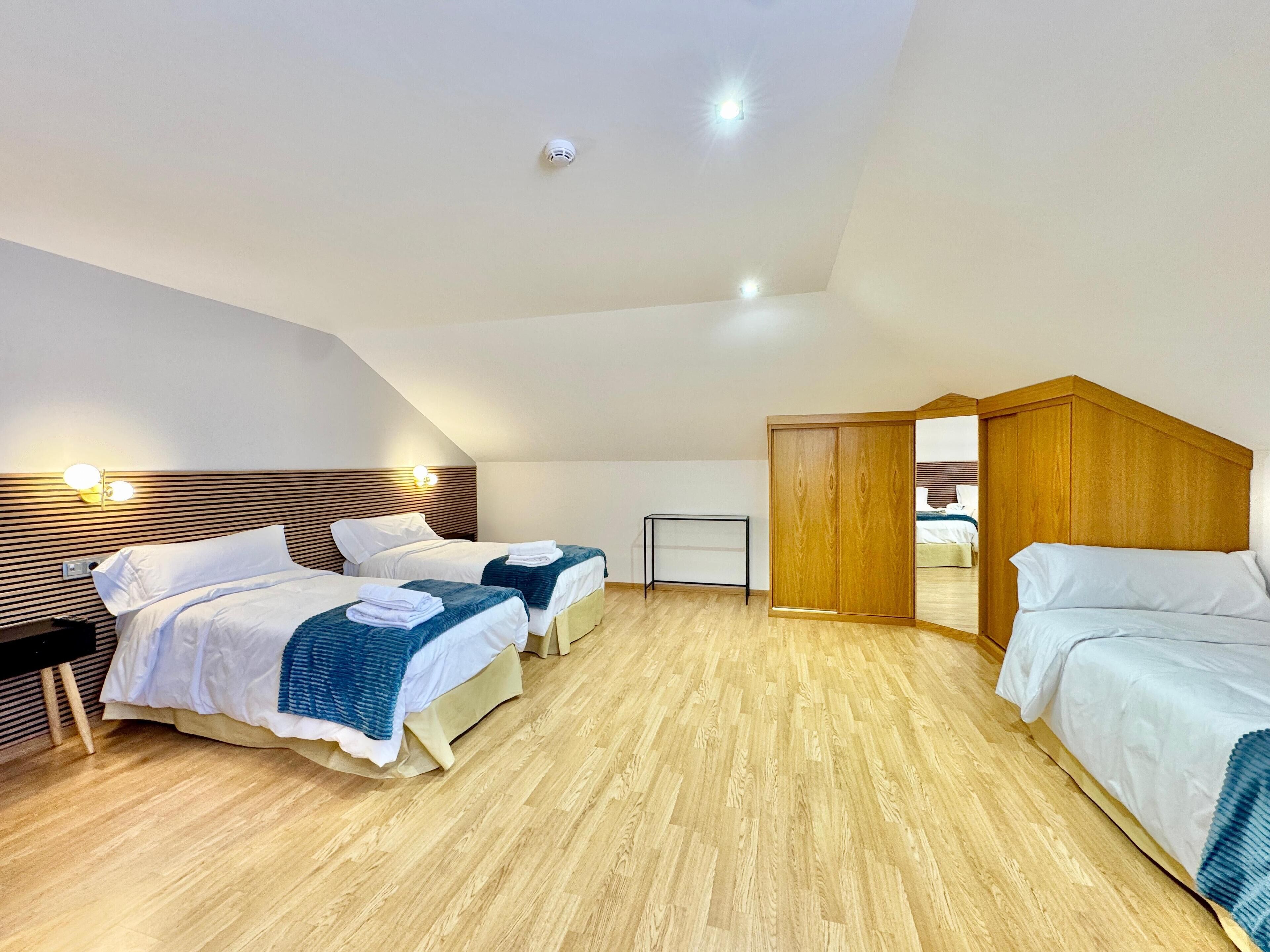Habitación de hotel con dos camas, cabecero de madera, una mesita pequeña y un armario de madera.