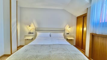 Quarto de hotel com uma cama grande, duas mesas de cabeceira com abajures, um guarda-roupa de madeira e uma janela com cortinas finas.