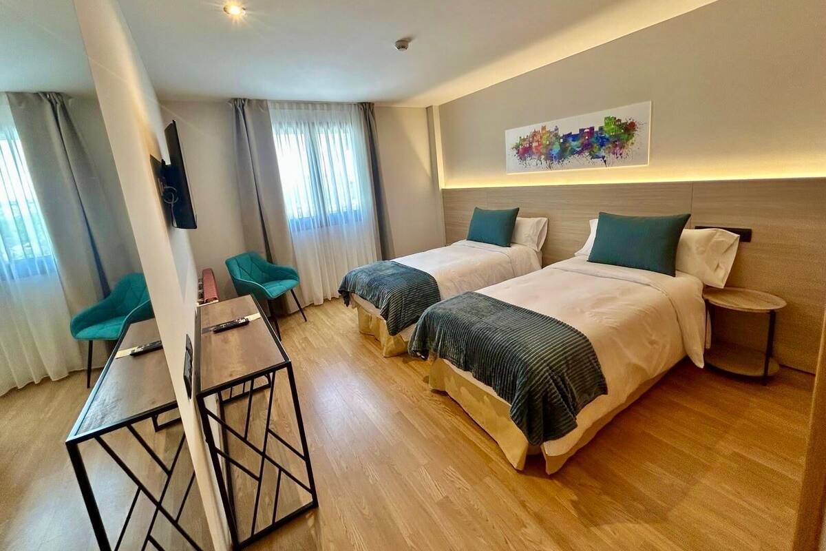 A hotel room with two beds, a desk, a chair, and a small round table.