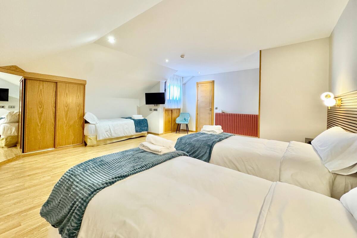 A hotel room with two beds, a TV, a chair, and a wardrobe.