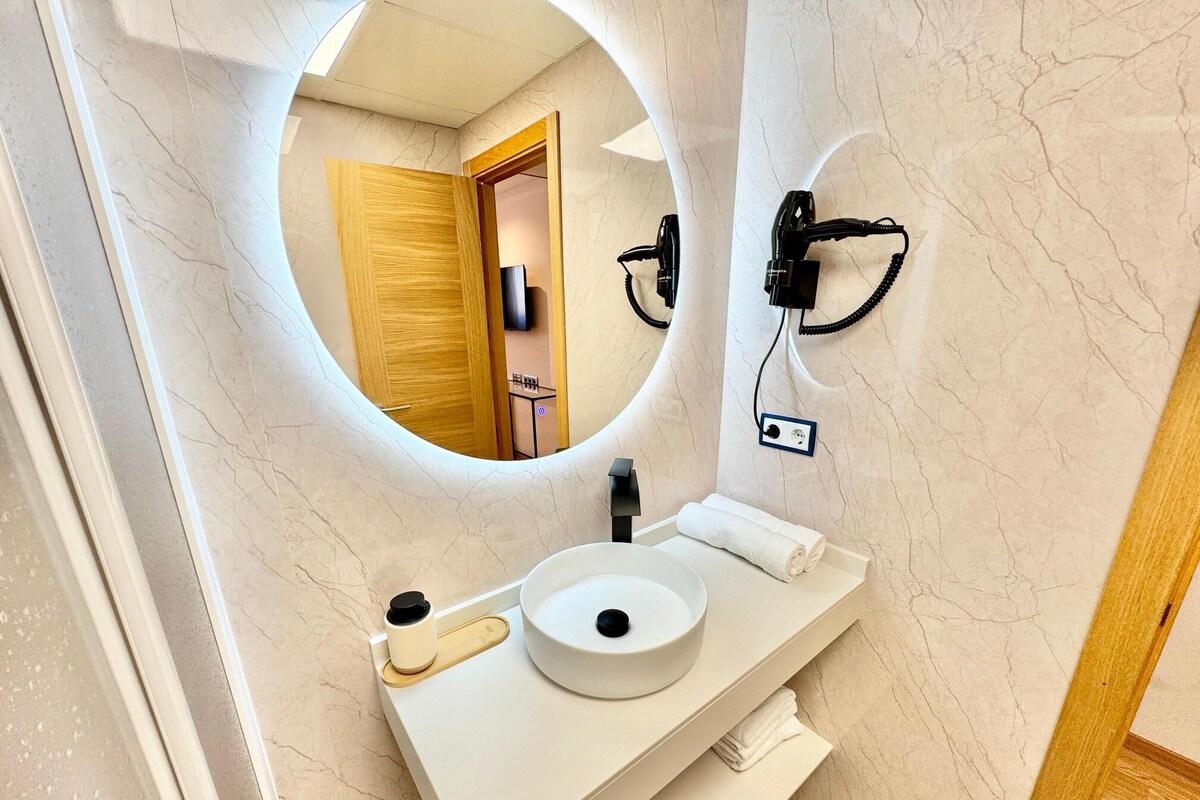 A bathroom with a round mirror, a sink with a towel, and a wall-mounted hairdryer.