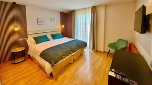 A hotel room with a large bed, a small table, a chair, a TV, and a window with curtains. - Hotel Diró (Avila)