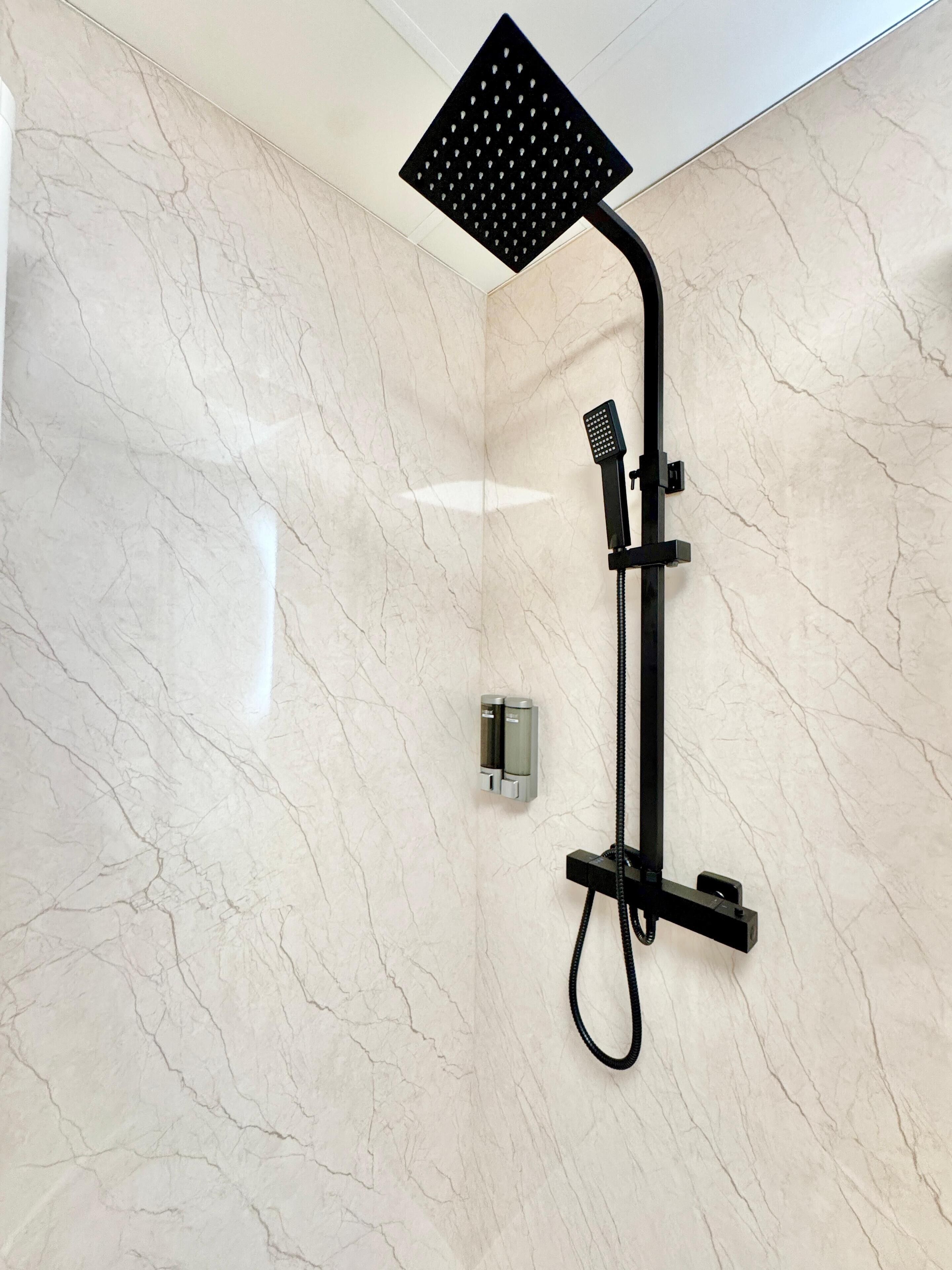 A modern bathroom with a marble wall, a black showerhead, and a handheld shower attachment.