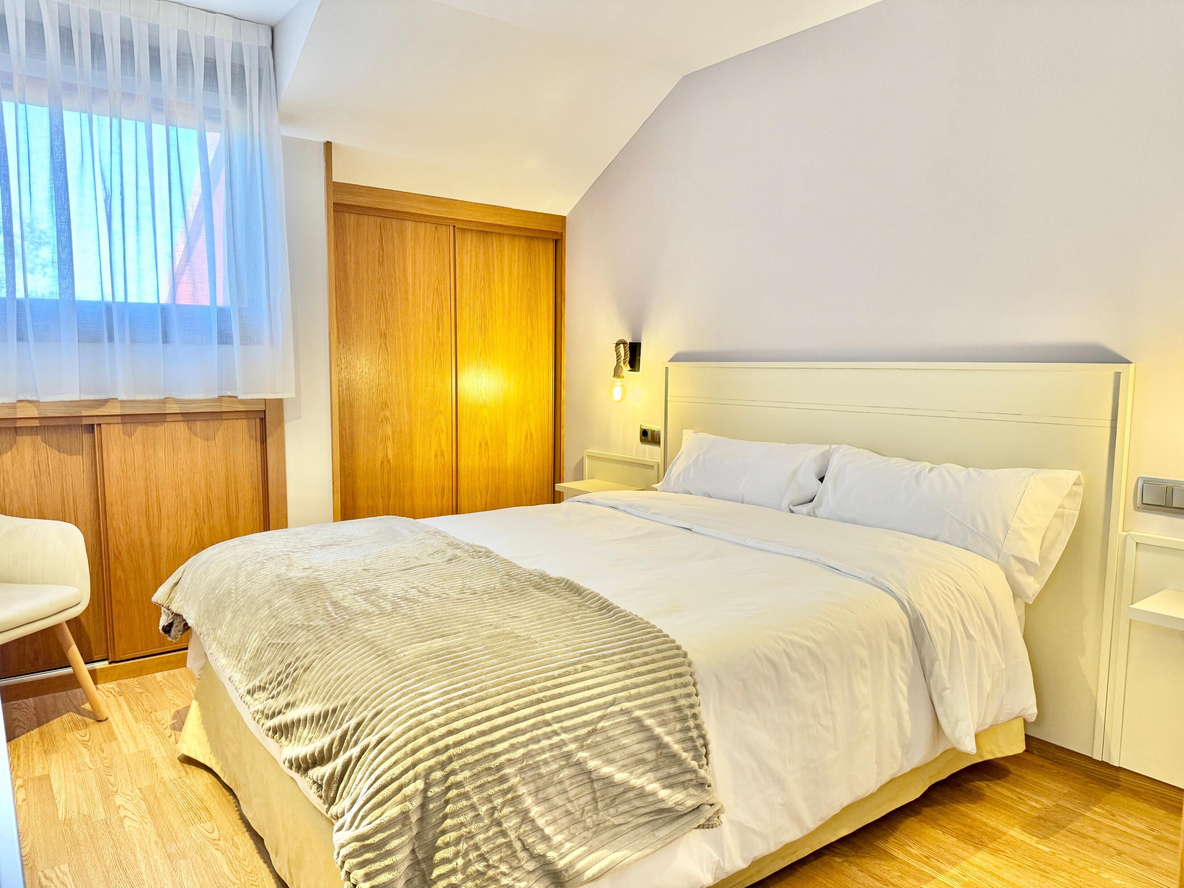A neatly arranged bedroom with a bed, a chair, a wooden wardrobe, and a nightstand with a lamp.