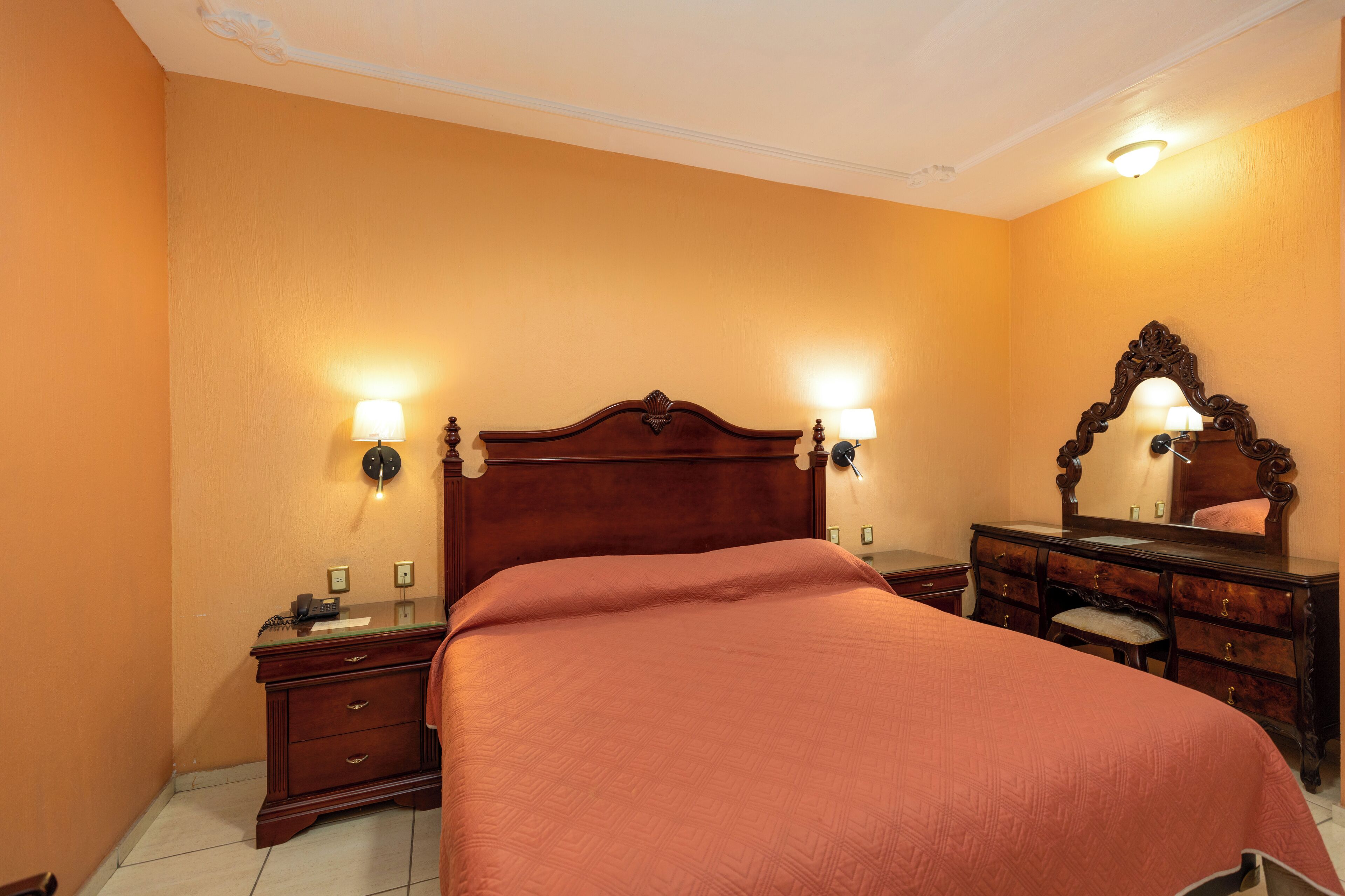 Un dormitorio con una cama grande, un aparador de madera, un espejo y dos lámparas de pared.