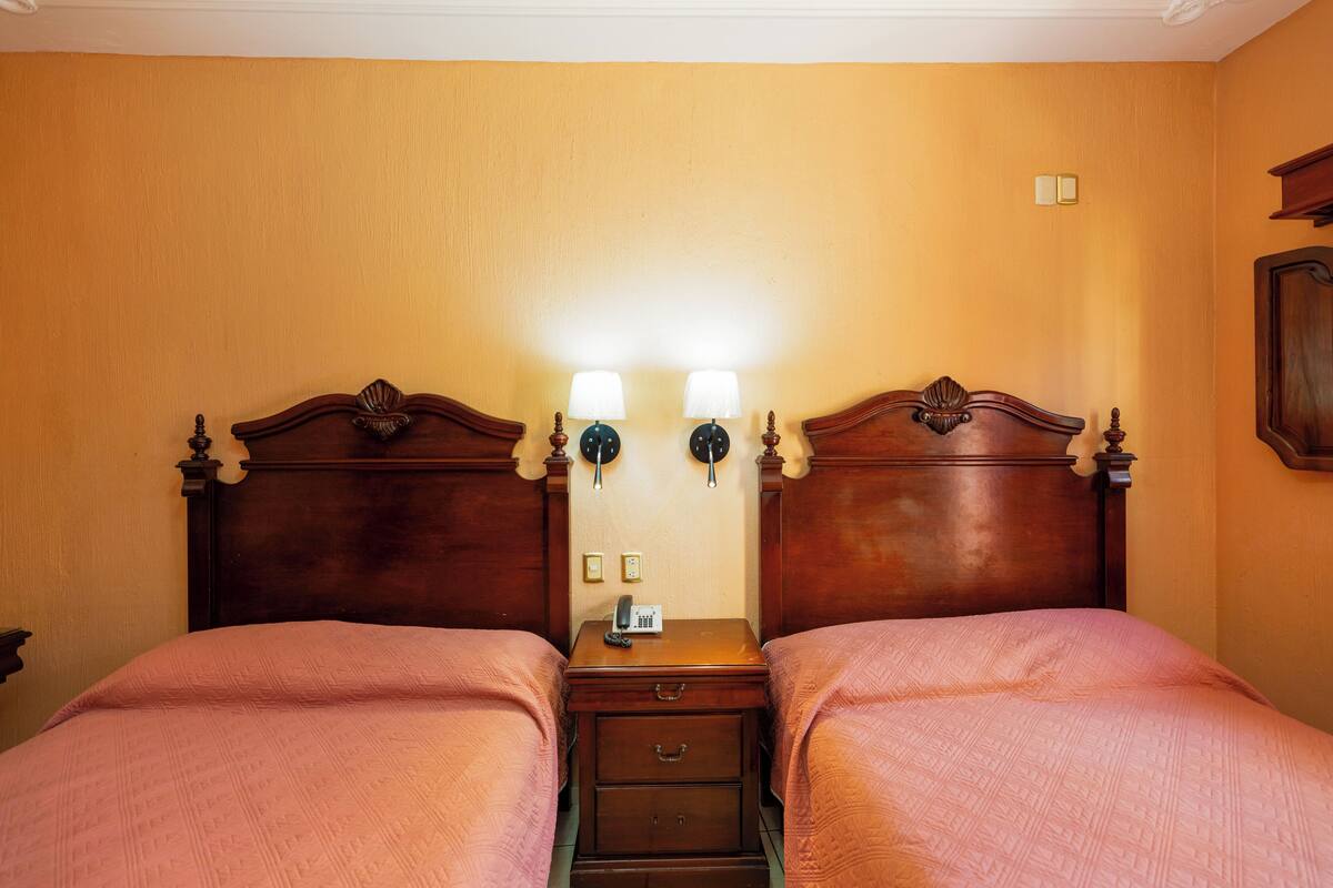 Une chambre double avec deux lits, une table de chevet, un téléphone et des lampes fixées au mur.