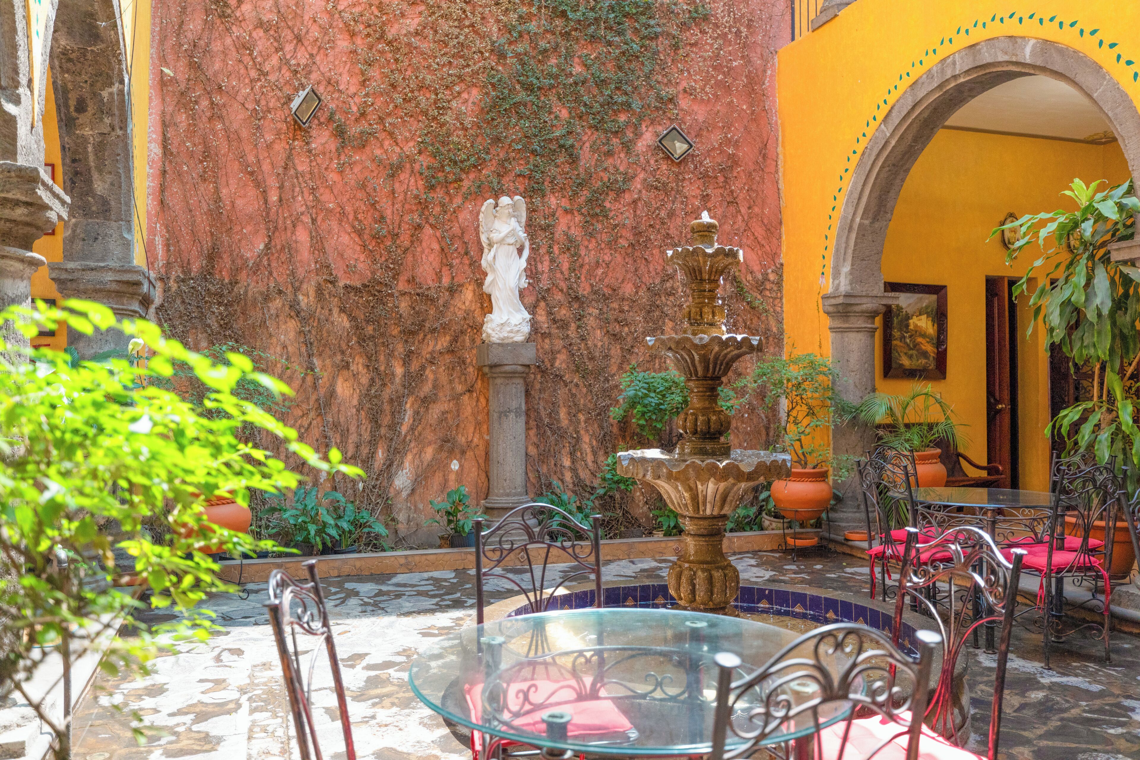 A courtyard with a glass table, metal chairs, a fountain, and potted plants.