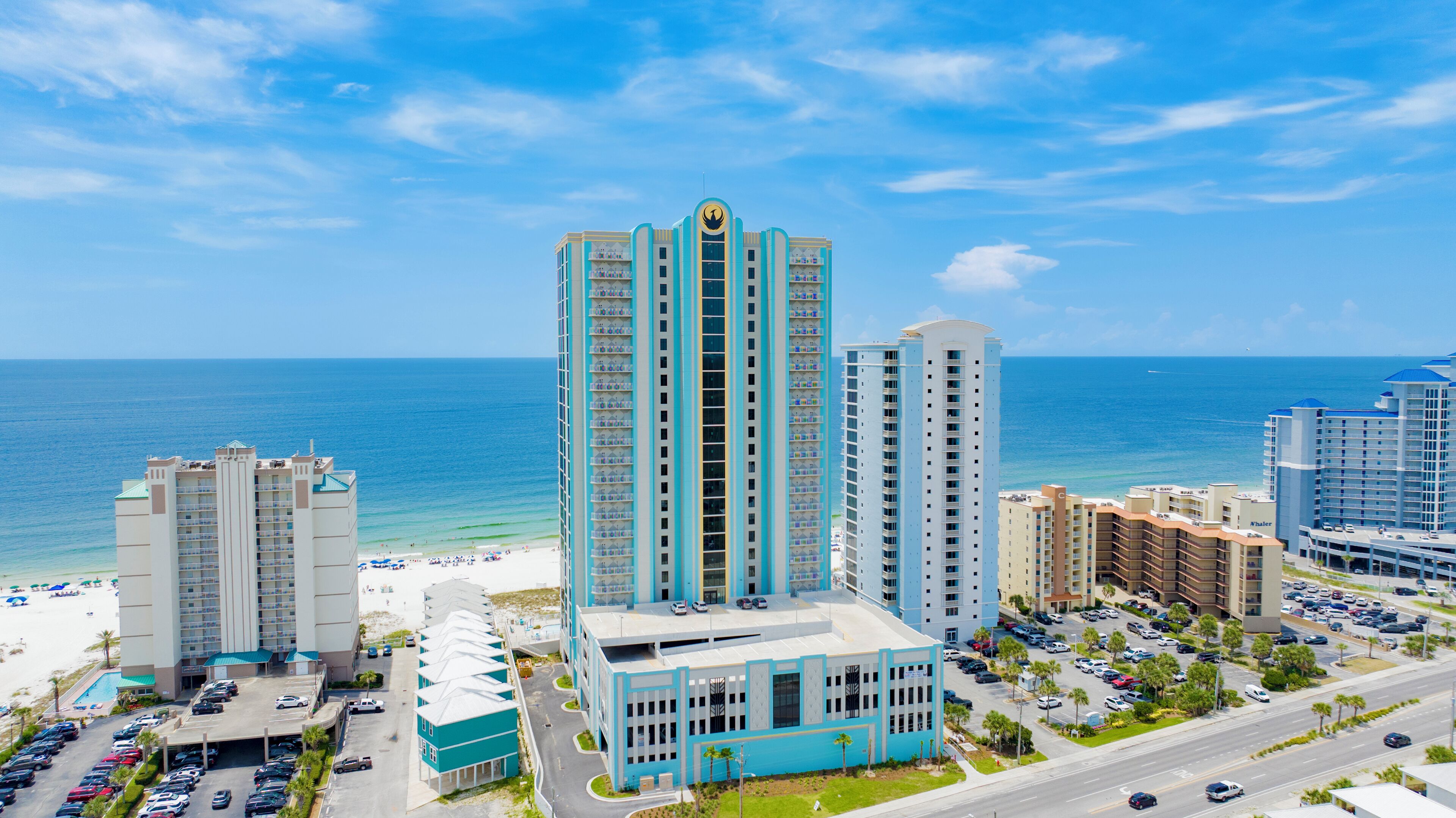 Un hotel de gran altura con una torre central, playa y estacionamiento.